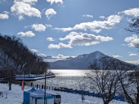 冬の支笏湖温泉の湖畔。雪の上から見る支笏湖と風不死岳、左に山線鉄橋（2025年2月8日）