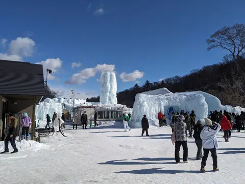 千歳・支笏湖氷濤まつりの会場。青空の下に氷のオブジェが並び、中央に大氷柱（2025年2月8日）